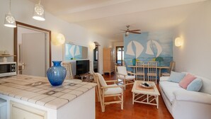A living room with a white sofa, a coffee table, and a TV. There is a painting of sailboats on the wall. - Casa Graziana by Wonderful Italy (Olbia)