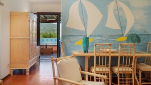 A dining area with wicker chairs and a table, a wooden cabinet, and a mural of sailboats on the wall. - Casa Graziana by Wonderful Italy (Olbia)