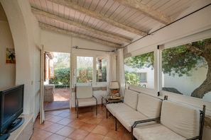 A room with a sofa, chairs, a TV, and a window overlooking greenery. - Casa Pierina by Wonderful Italy (Olbia)