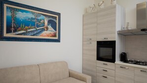 A modern kitchen with a built-in oven and stove, a beige sofa, and a painting of a coastal landscape. - Casa Perla by Wonderful Italy (Olbia)