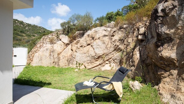 A lounge chair with a cushion and a book, positioned on a grassy area beside a rocky cliff. - Casa Perla by Wonderful Italy (Olbia)