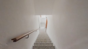 Una escalera con barandilla que lleva a una habitación luminosa con ventana y cortina.
