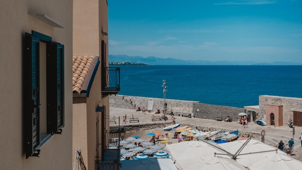 Un pueblo costero con un muro de piedra, sombrillas de playa y una vista despejada del mar.
