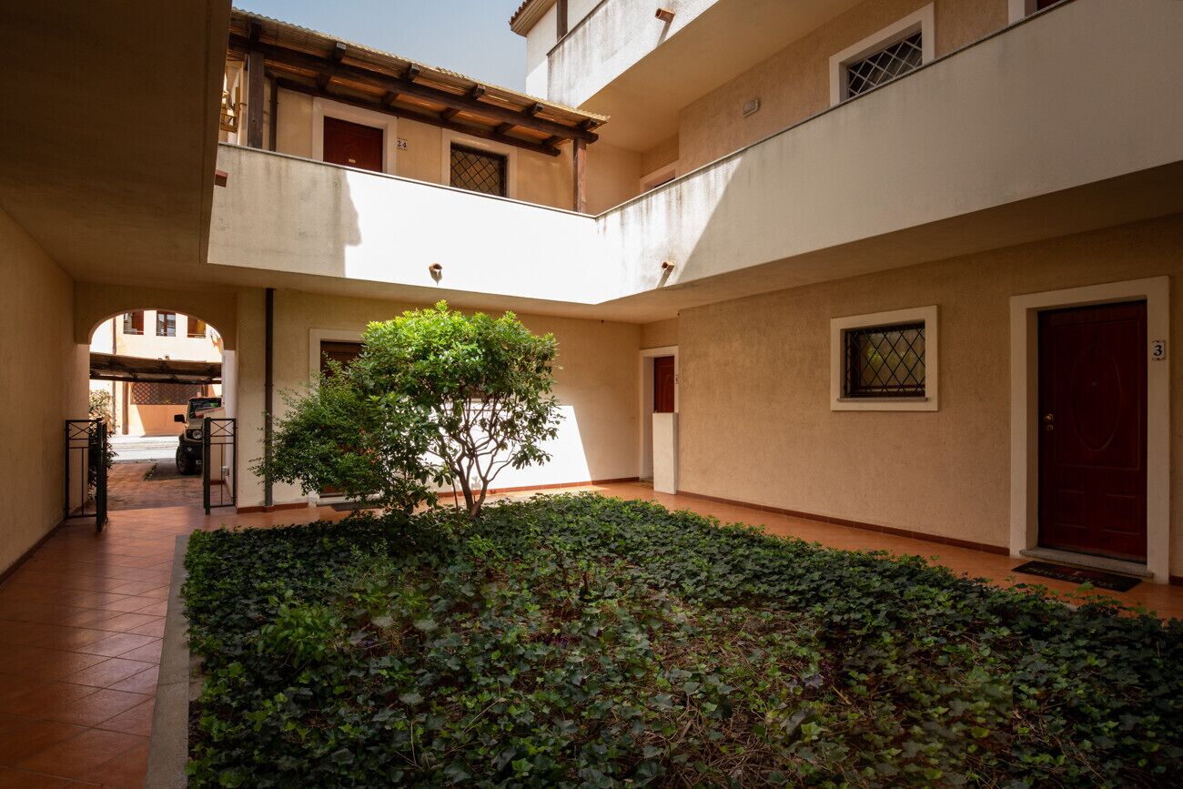 A courtyard with a tree, a scooter, and a building with a red door.