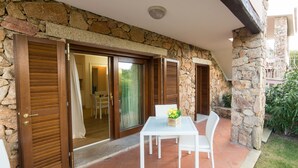 A patio with a white table and chairs, a stone wall, and wooden shutters. - Casa Natal a by Wonderful Italy (Olbia)