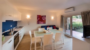 A modern kitchen with white cabinets, a blue countertop, and a dining area with white chairs and a glass table. - Casa Natal a by Wonderful Italy (Olbia)