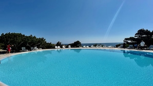 En stor, klarblå pool med vita solstolar och utsikt över havet.