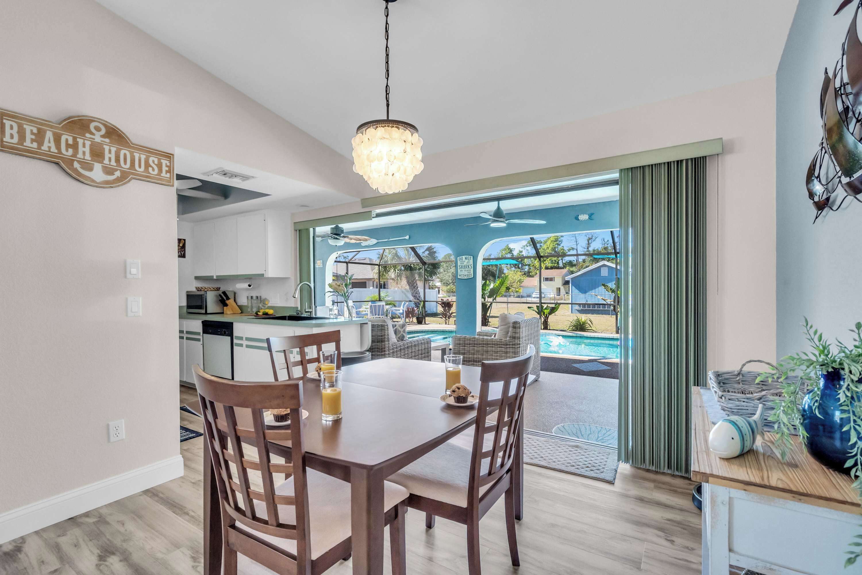 A dining area with a table and chairs, a kitchen in the background, and a view of a pool and outdoor seating area.