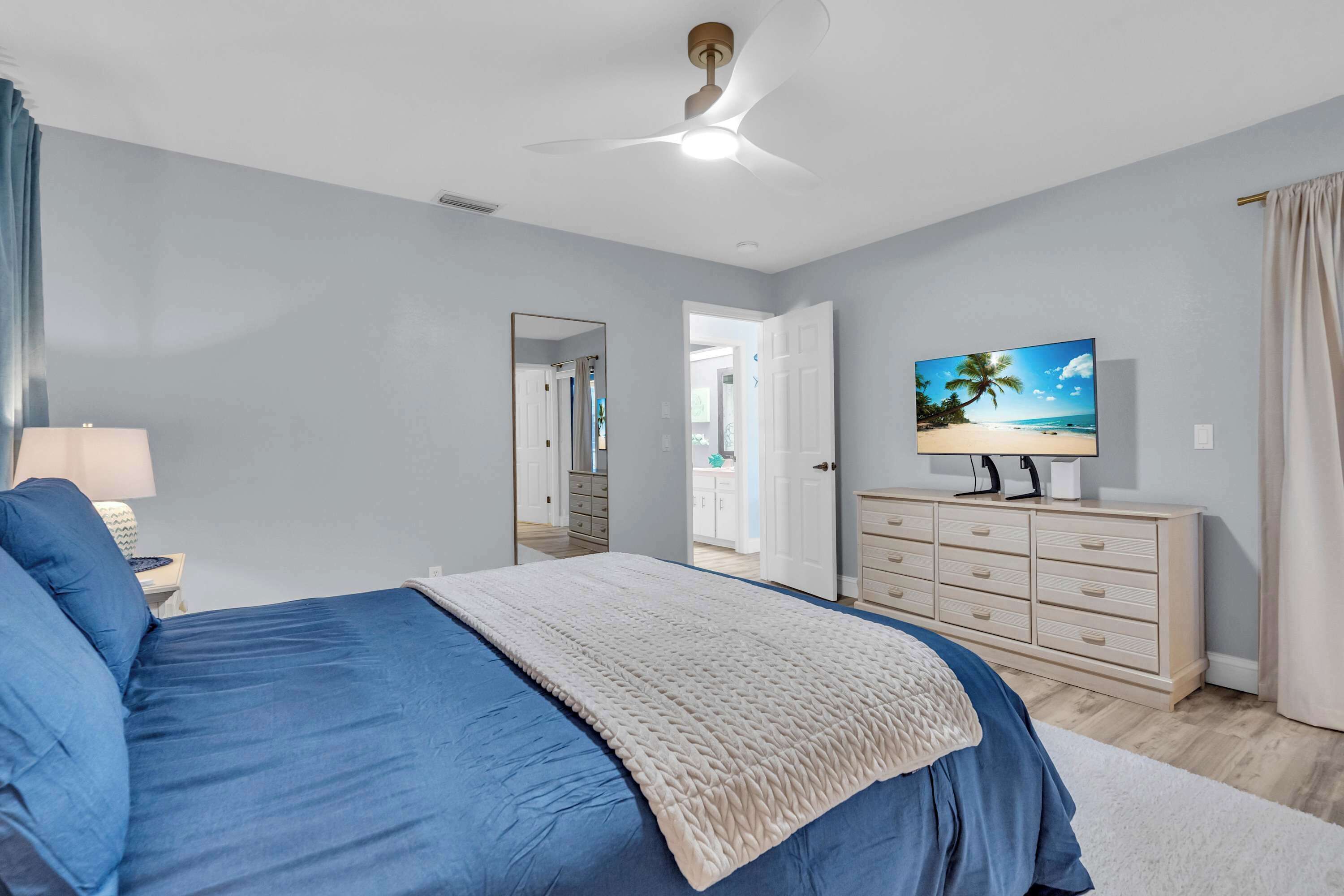 A bedroom with a bed, a TV, a dresser, and a ceiling fan.