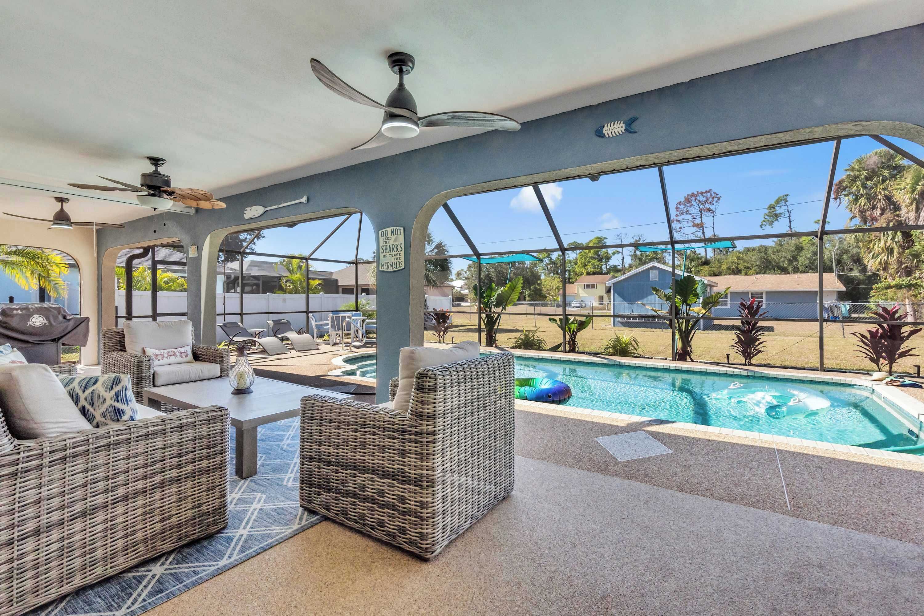 A poolside area with wicker furniture, ceiling fans, and a view of the surrounding neighborhood.