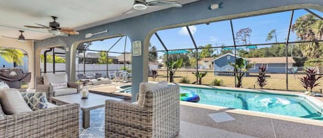 A poolside area with wicker furniture, ceiling fans, and a view of the surrounding neighborhood.