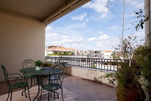 A balcony with a table and chairs, potted plants, and a view of buildings in the distance. - Pedra Mendalza Apartment by Wonderful Italy (Olbia)