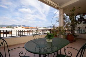 A balcony with a green metal table and chairs, potted plants, and a view of buildings and mountains in the distance. - Pedra Mendalza Apartment by Wonderful Italy (Olbia)