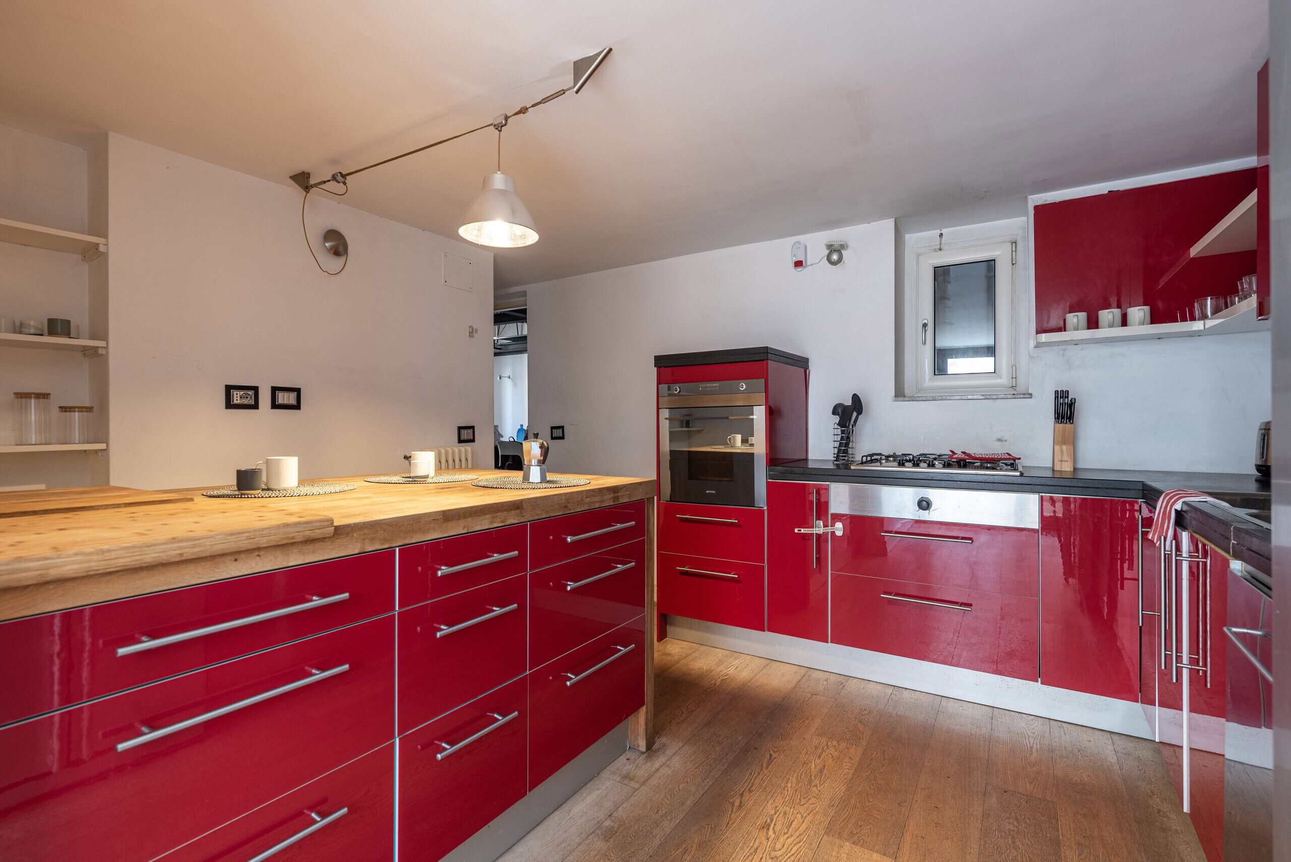 Una cucina moderna con mobili rossi, un piano di lavoro in legno e un forno integrato.