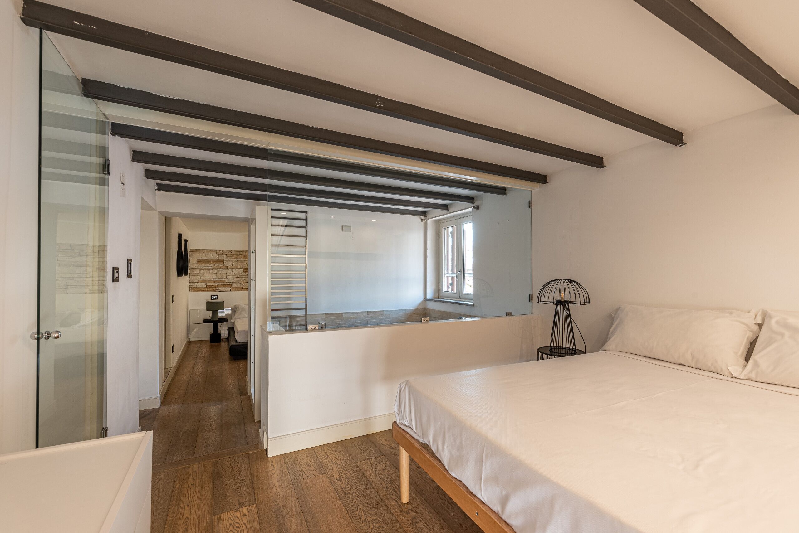 A modern bedroom with a large bed, a glass shower enclosure, and a built-in desk area.