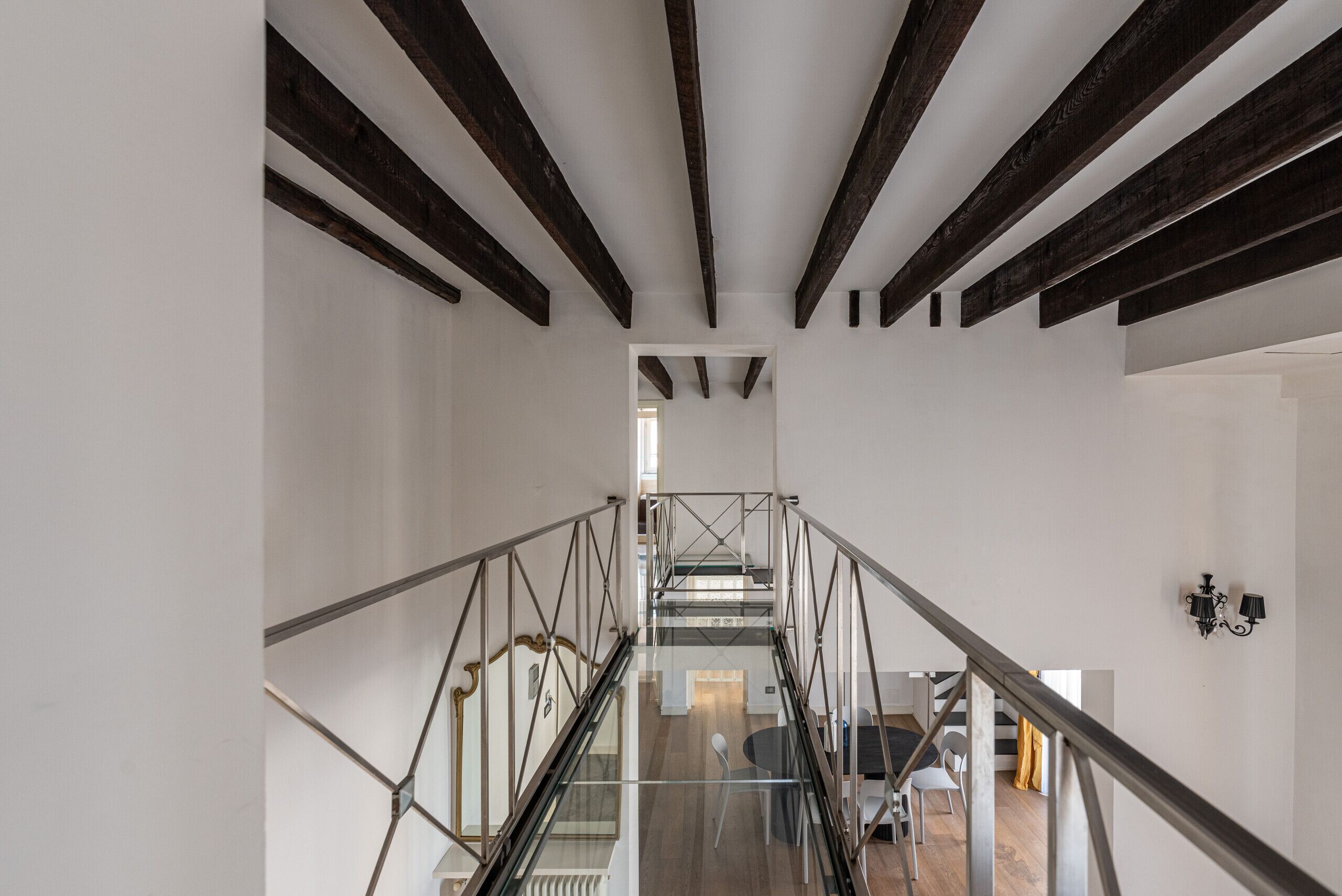 Un interior moderno con escalera, barandillas de vidrio y un comedor con sillas y mesa.