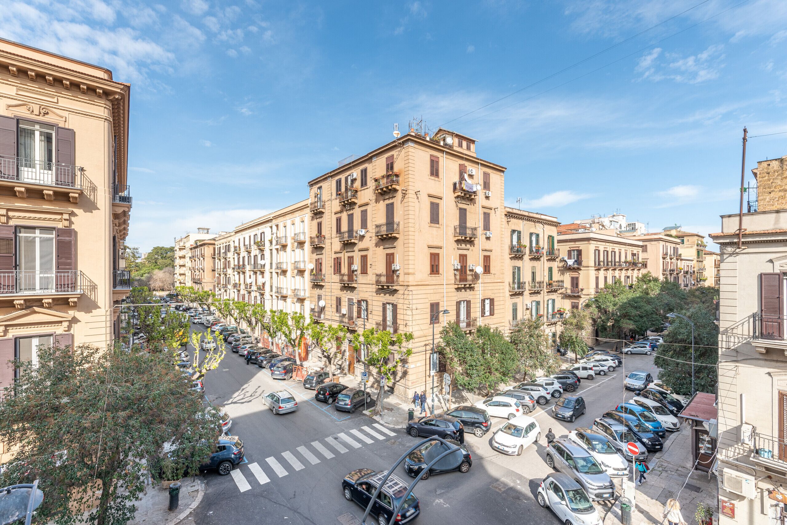 Un edificio de varios pisos con balcones, autos estacionados y un paso de peatones.
