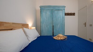 Quarto com cabeceira de madeira, colcha azul, almofadas brancas e guarda-roupa azul.