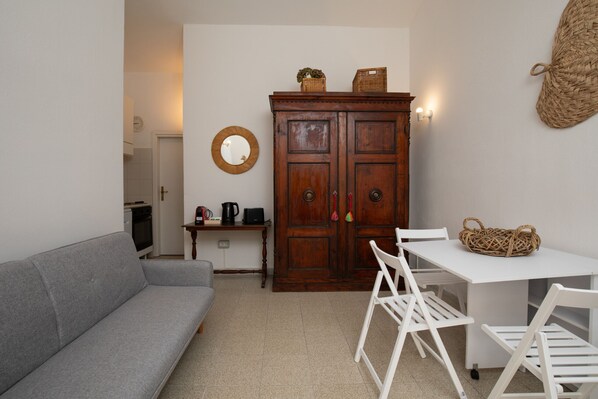 A compact living space with a grey sofa, a wooden cabinet with baskets, a small table with chairs, and a woven basket on the table. - Casa Girgolu by Wonderful Italy (San Teodoro)