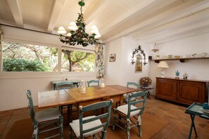 A dining area with a wooden table, chairs, a chandelier, and a view of trees through a window. - Villa Ippocampo by Wonderful Italy (Olbia)