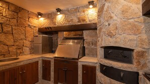 Cocina con paredes de piedra, electrodomésticos integrados, armarios de madera y una chimenea de piedra.