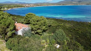 Une propriété située sur la côte, avec un bâtiment à toit rouge entouré d’une végétation luxuriante et donnant sur une mer d’un bleu limpide.