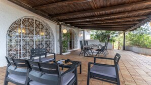 Een terras buiten met houten meubels, een barbecue en een decoratieve metalen poort.