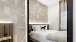 A modern hotel room with a geometric-patterned wall, a bed with white bedding, and a bedside table. - The Weekender Hotel (San Juan)