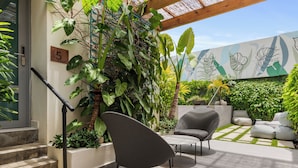 A modern outdoor patio with a sofa, a chair, and a table. There is a staircase leading to an upper level, and a wall with a number sign. - The Weekender Hotel (San Juan)