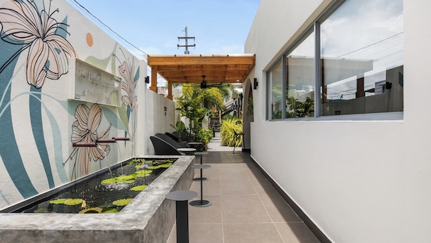 A modern outdoor corridor with a decorative wall, a water feature, seating, and a wooden pergola. - The Weekender Hotel (San Juan)