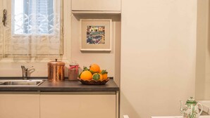 A kitchen with a sink, a copper-colored container, a bowl of oranges, a framed artwork, and a teapot on the counter. - Suite Granatelli by Wonderful Italy (Palermo)