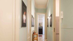 A narrow hallway with light green walls, wooden flooring, and framed pictures on the walls. There is a small wooden table with a chair in the middle of the hallway. - Suite Granatelli by Wonderful Italy (Palermo)