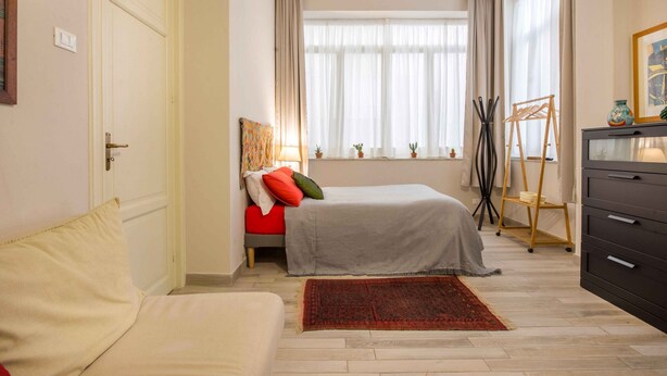 A bedroom with a bed, a sofa, a window with curtains, a small table, and a dresser. - Suite Granatelli by Wonderful Italy (Palermo)