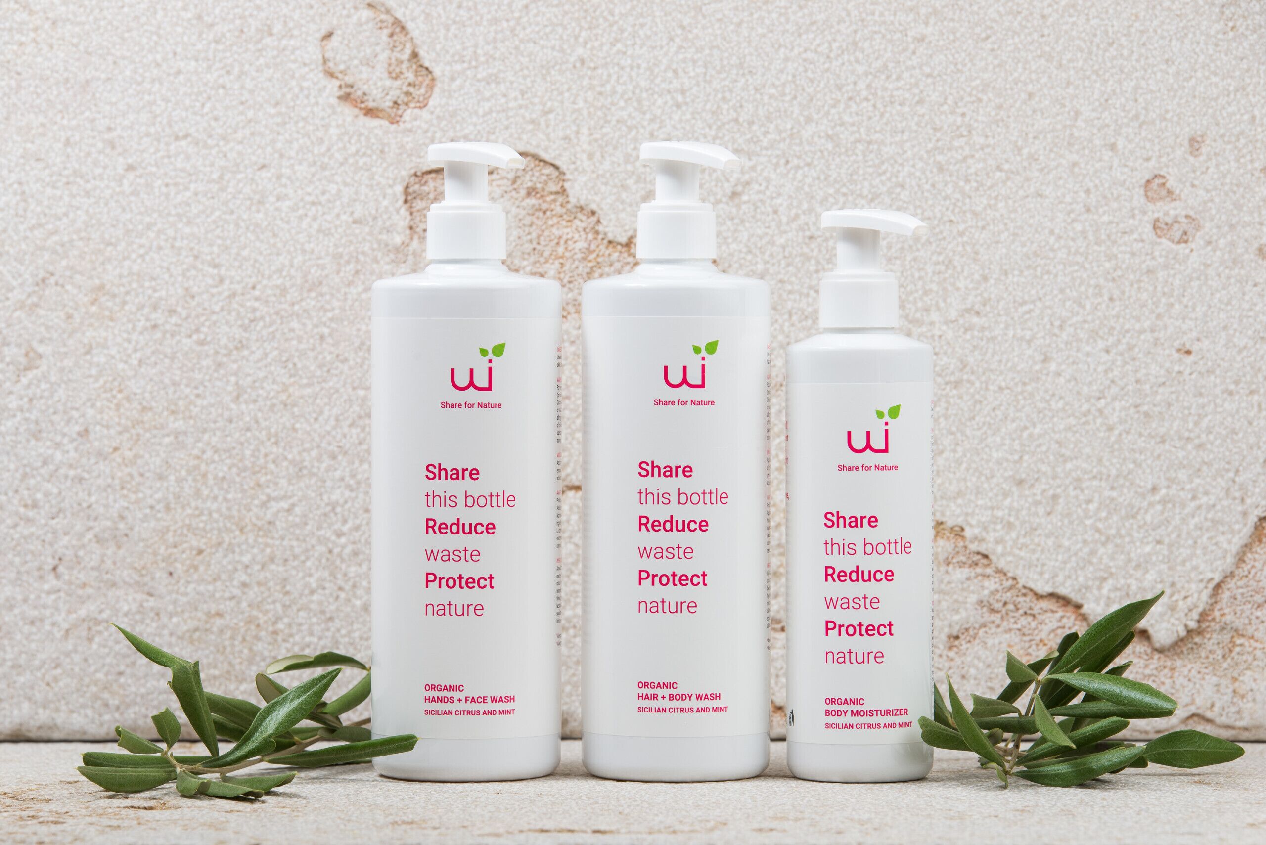 Three white bottles with pump dispensers, each labeled "Share for Nature" and "Reduce waste Protect nature." They are placed on a textured surface with green leaves beside them.