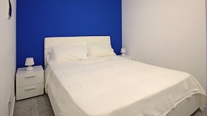 Ein Schlafzimmer mit einem weißen Bett, zwei Nachttischen und einer blauen Akzentwand.