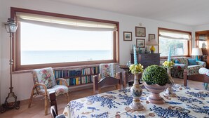 Une pièce dotée d’une grande fenêtre, d’une bibliothèque, d’une table à manger recouverte d’une nappe à motifs floraux et d’une lampe.