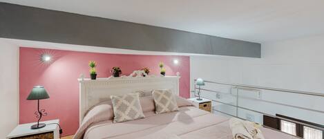 A bedroom with a bed, bedside tables, a lamp, a wall-mounted shelf with plants, and a window with a view.