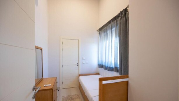 Une petite chambre avec un lit simple, une tête de lit en bois, une table de chevet, une armoire et une porte.