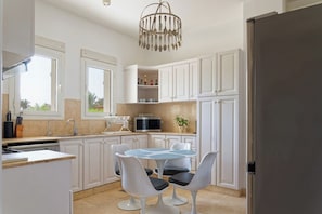 A modern kitchen with white cabinets, a dining table with chairs, a microwave, and a chandelier. - VESTA - Gouna Residence  (El Gouna)