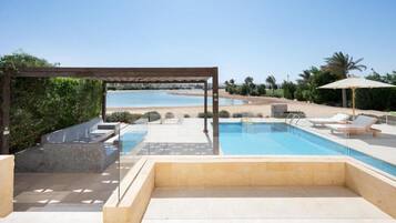 A pool area with a pergola, lounge chairs, and a view of the beach.