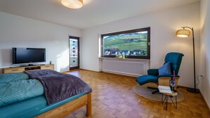 Une chambre moderne équipée d’une télévision, d’un lit, d’une chaise, d’une fenêtre donnant sur un beau paysage et d’une lampe sur pied.