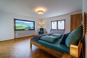 Ein Zimmer mit einem Bett, einem Fernseher, einem Sessel und Blick ins Freie.