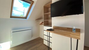 A modern room with a skylight, a flat-screen TV mounted on the wall, a wooden shelf with a remote control, and a small bottle of hand sanitizer. - Cozy Studio near Quimper Train Station – Modern & Bright (Quimper)