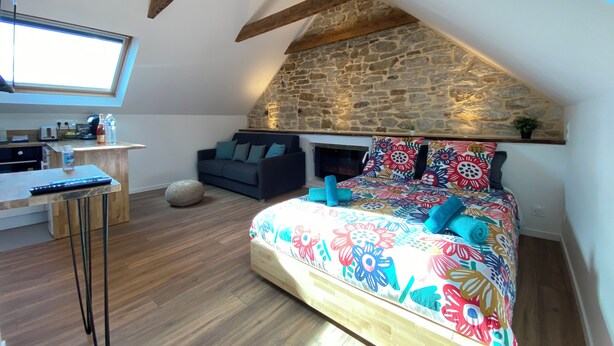 A cozy loft bedroom with a sloped ceiling, stone wall, and a bed with colorful floral bedding. - Cozy Studio near Quimper Train Station – Modern & Bright (Quimper)