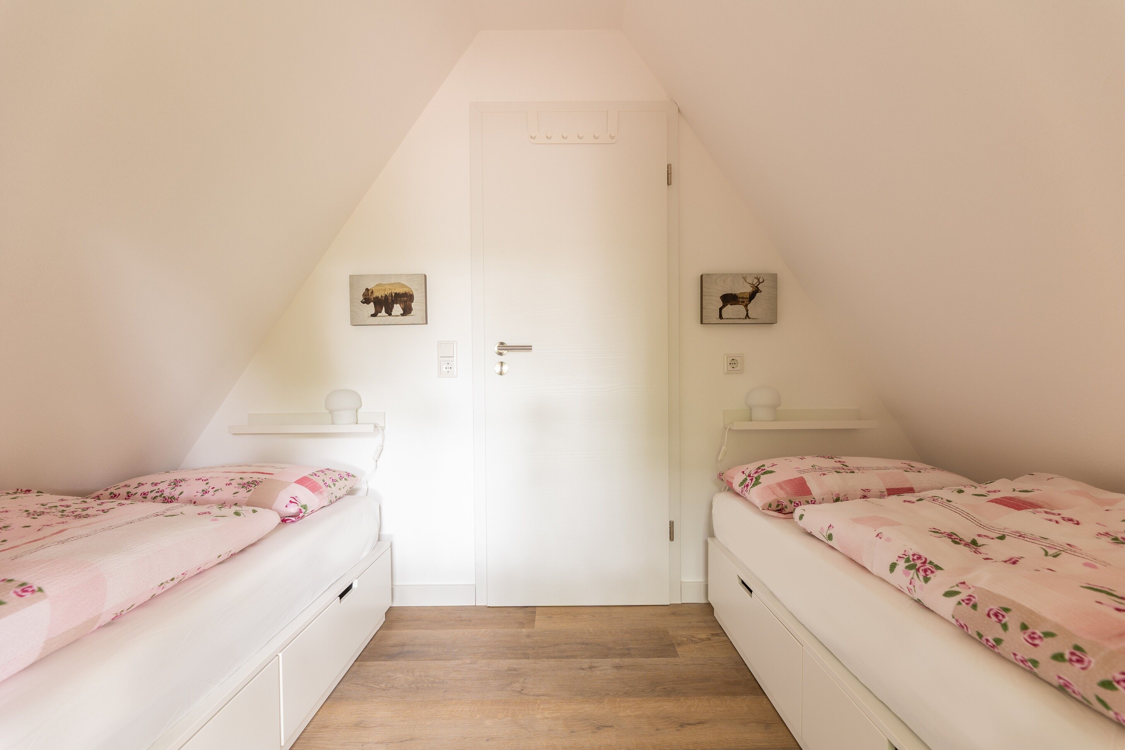 A bedroom with two beds, a white door, and a small shelf with a picture.