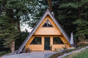 A triangular wooden cabin with a porch, large windows, and a door.