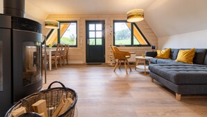 Uma sala de estar aconchegante com lareira, sofá, mesa de jantar e vista para o exterior através de grandes janelas.