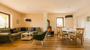 Ein gemütliches Wohnzimmer mit einer Couch, einem grünen Sessel, einem Esstisch mit Stühlen, einem Kamin und Holzwänden.