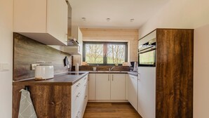 Eine kleine Küche mit Holzschränken, einem eingebauten Backofen und einem Fenster, das für natürliches Licht sorgt.