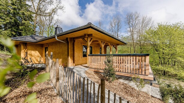 Eine Holzhütte mit Veranda, umgeben von Bäumen und einem Holzzaun.